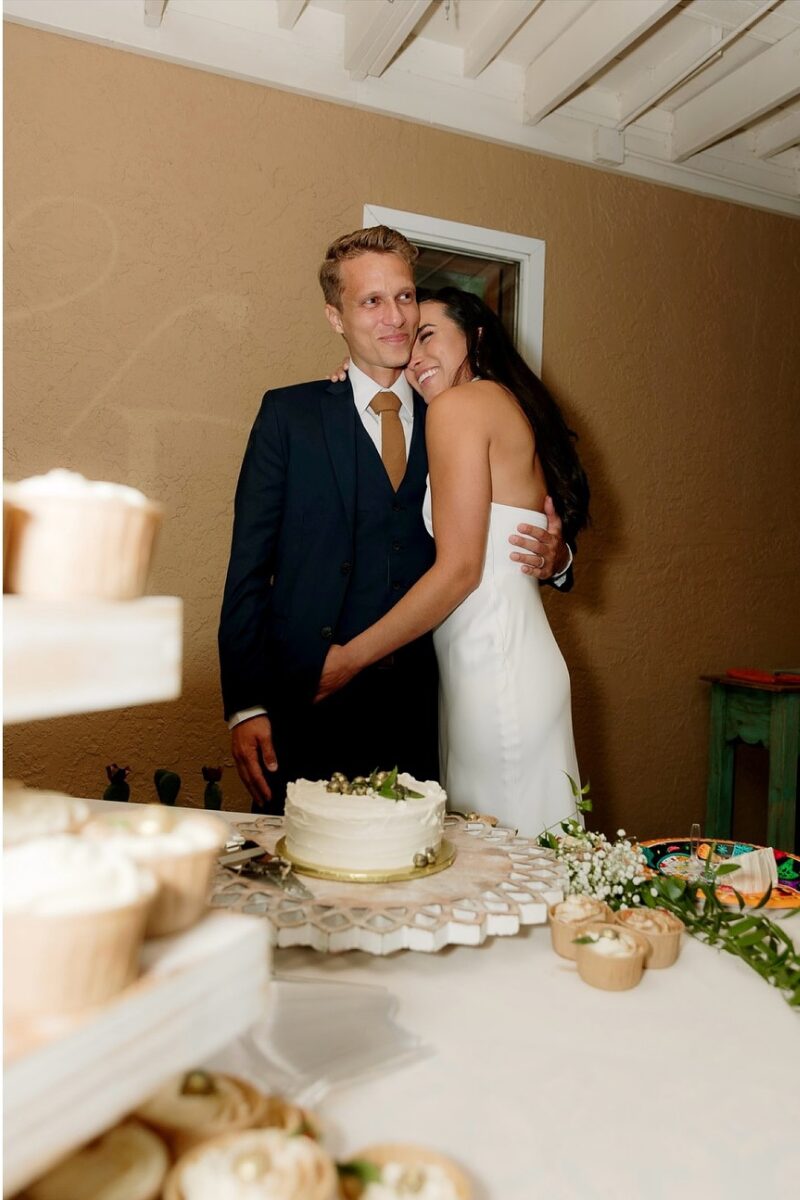 Newlyweds share a hug beside their wedding cake and cupcake display, a candid moment captured after they asked Serendipity Records Content Co. how long should you book a wedding day content creator.