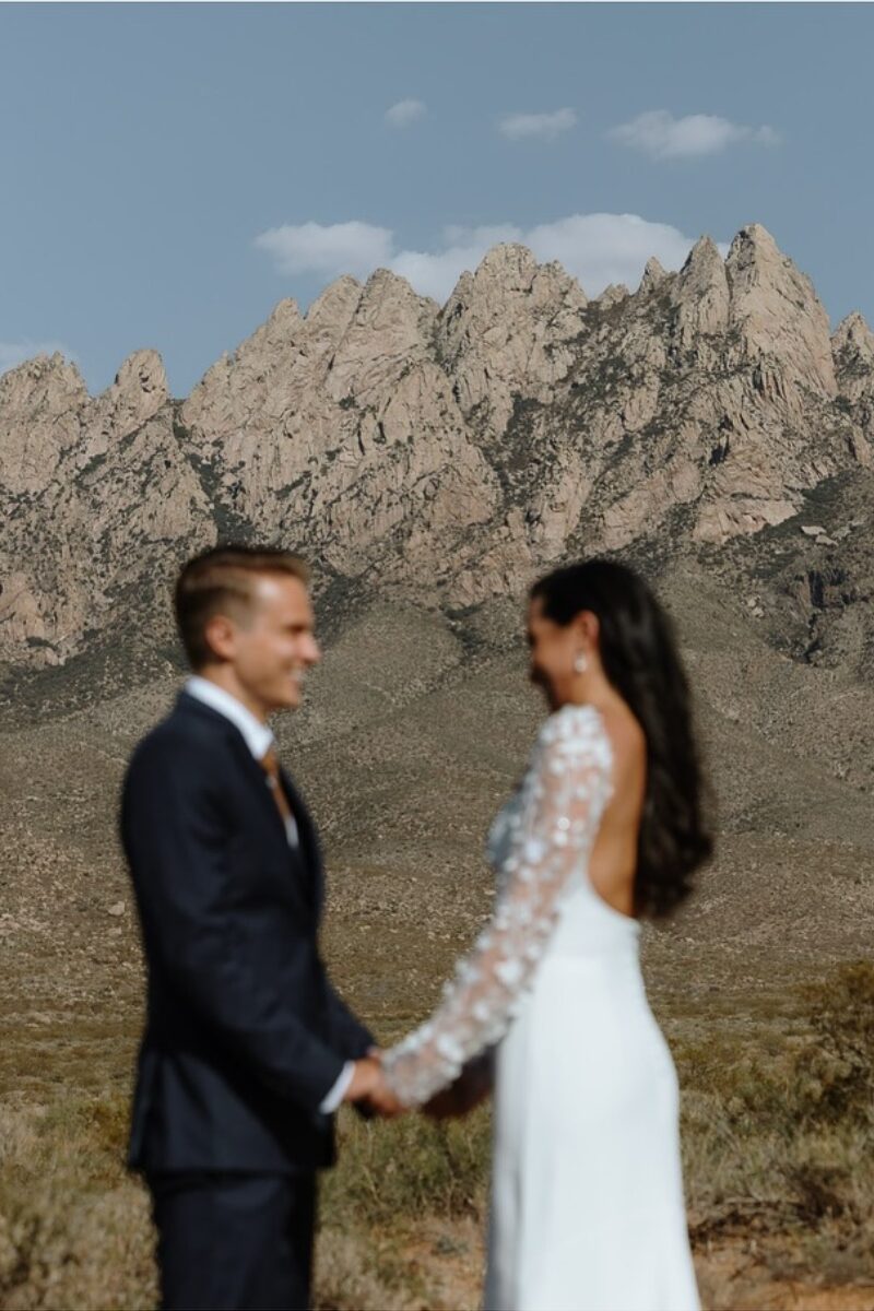 Bride and groom hold hands with the jagged Organ Mountains rising behind them.