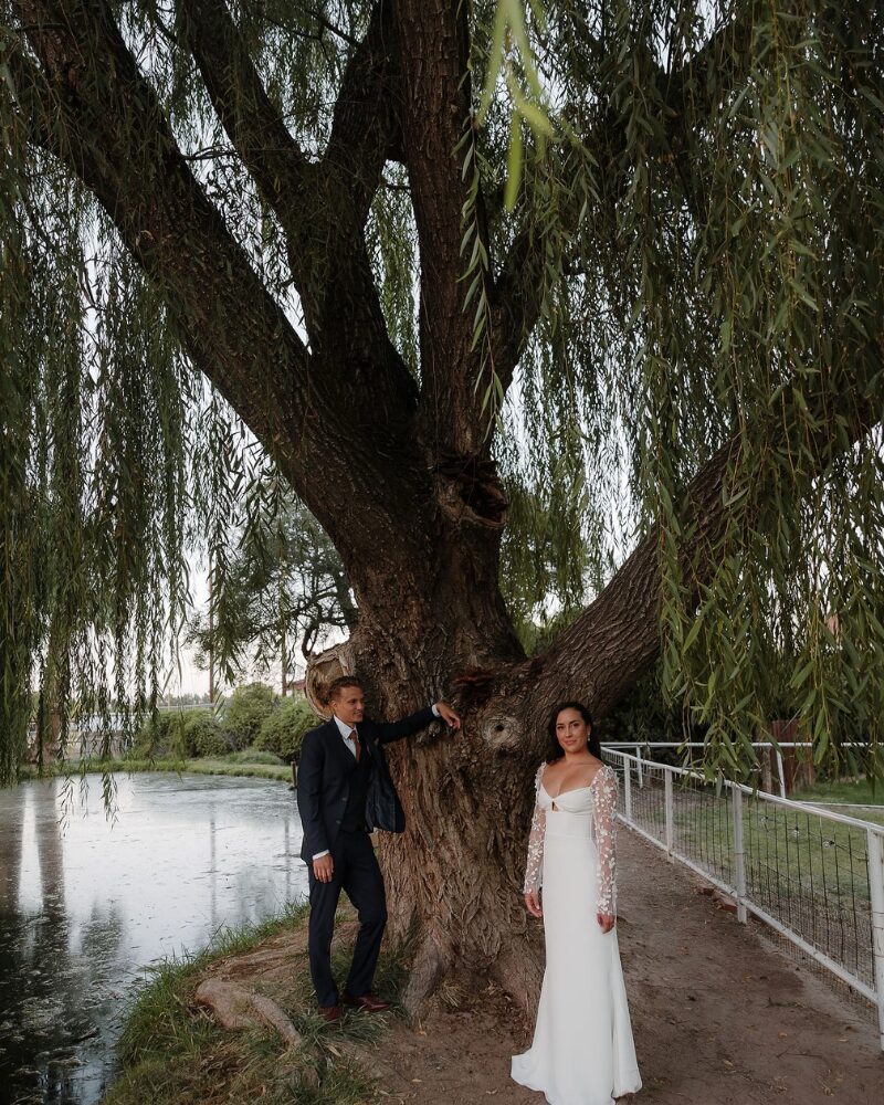 Bride and groom stand beneath a weeping willow tree at sunset, an in-between moment captured after they asked how long should you book a wedding day content creator.